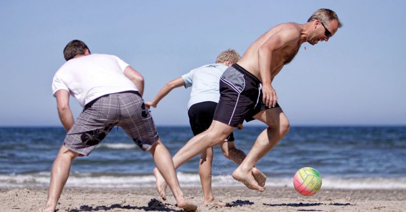 Dynamics - Men and Boy Playing Football on a Sandy Beach
