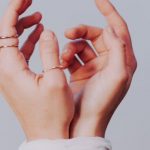 Injuries - Crop faceless female with stylish rings on fingers and hands tied with white bandage against gray background